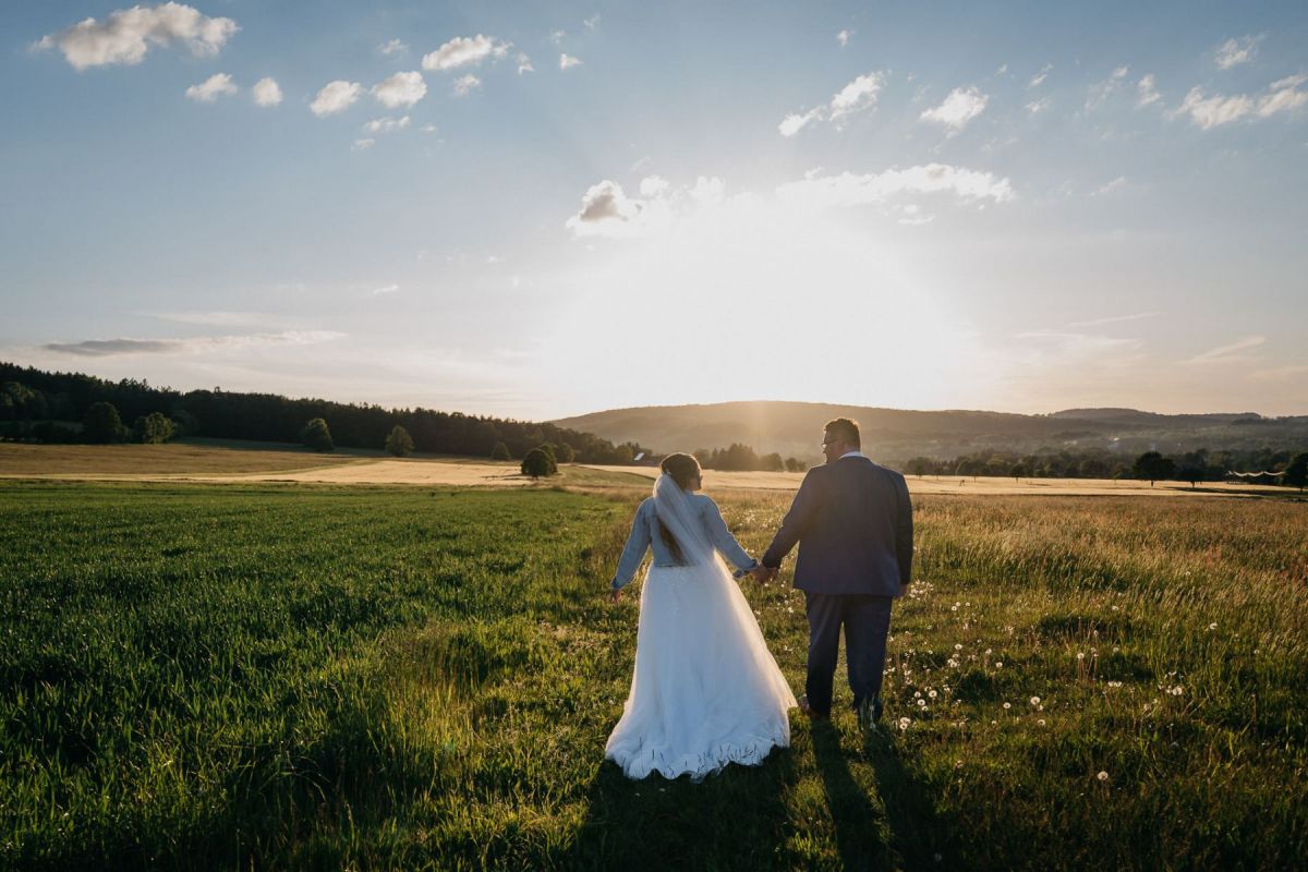 Janina und Tobias gehen bei Sonnenuntergang über eine Wiese in Waltersdorf