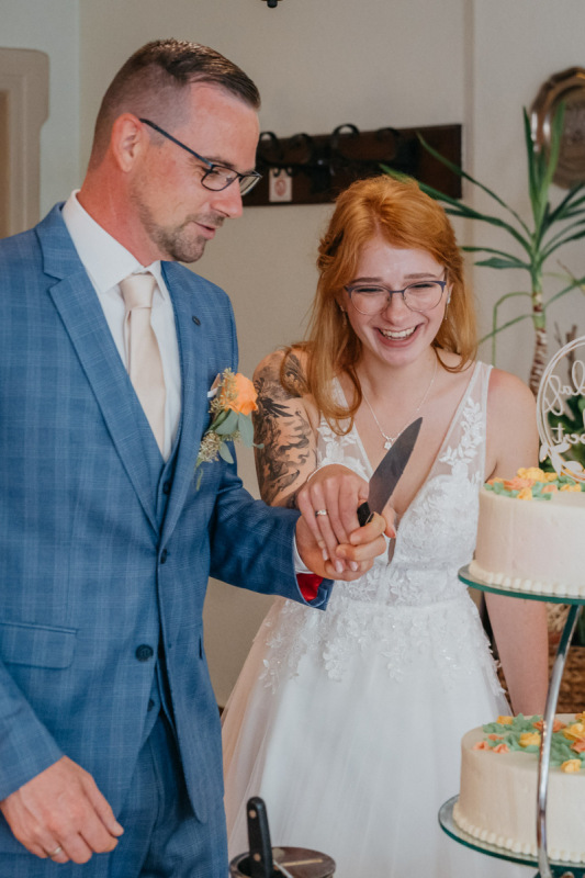 Linda und Robert lachen beim Anschneiden der Hochzeitstorte
