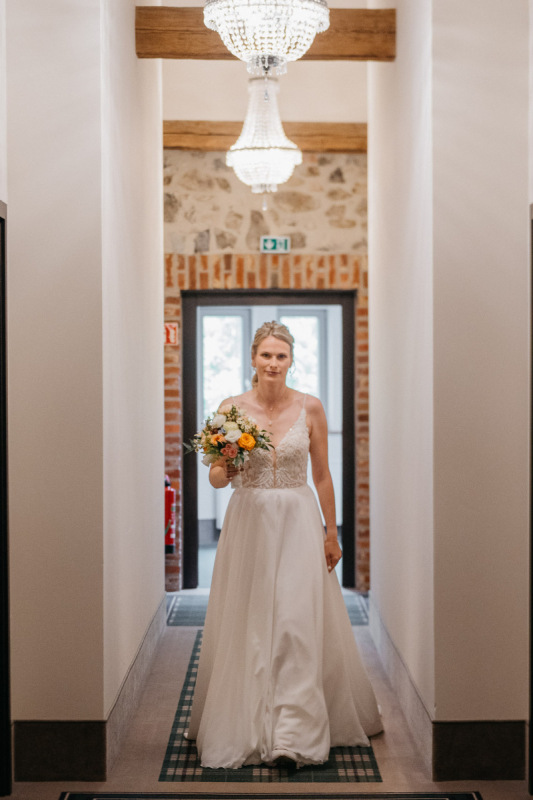 Sandra geht mit ihrem Brautstrauß zum First Look durch den Flur