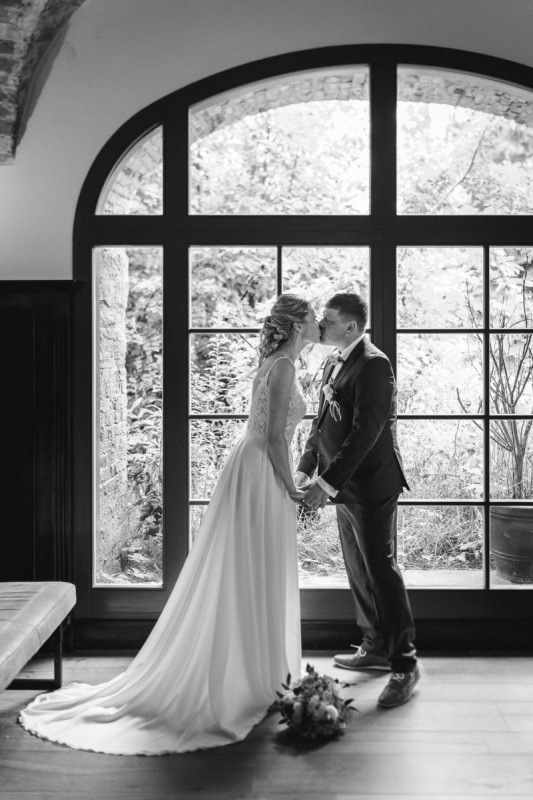 Sandra und Andy küssen sich am großen Fenster im Gut am See